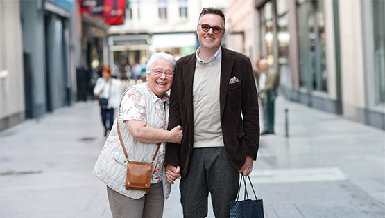 A senior citizen and younger person walk Dublin's city streets and smile at the camera