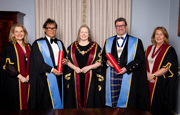 Five senior academics, three wearing maron graduation stoles and two wearing blue, smile for the camera.