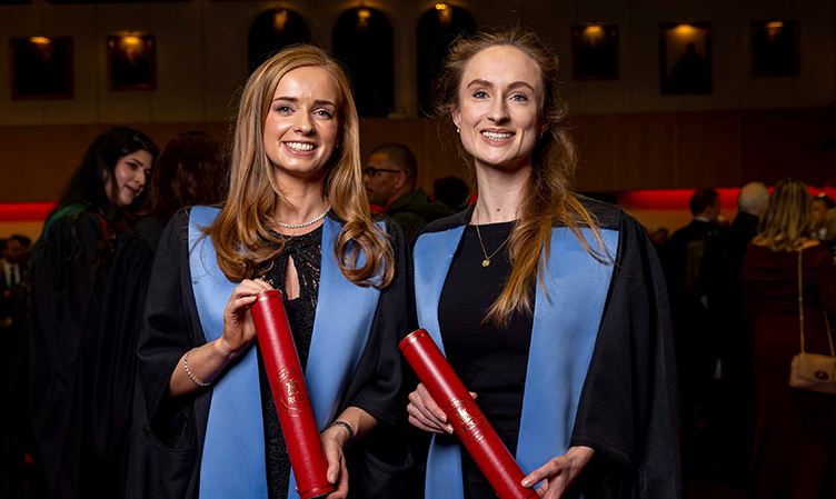 Two RCSI Fellows wearing graduation robes and holding scrolls smile for the camera