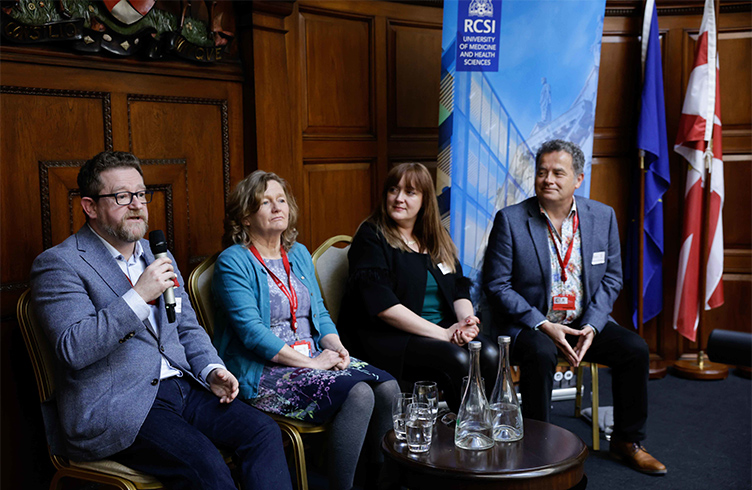 A man holds up a microphone to answer a question from the audience, while his three colleagues look on.