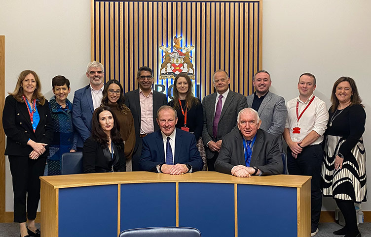 A large group of academics pose behind a blue desk and in front of the RCSI crest