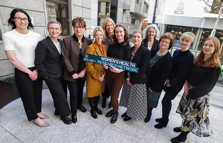 A large group of female academics pose outside RCSI on York Street with a sign that reads 'Women’s Health Research Network'.