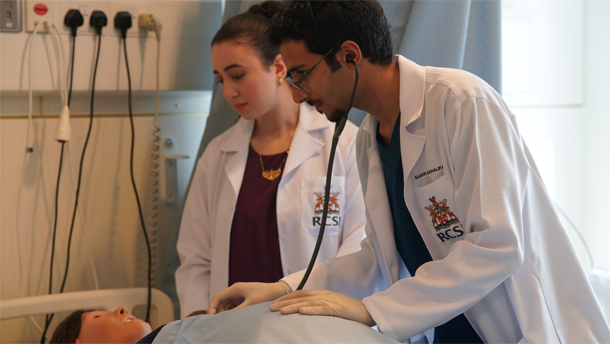 Two medical students in white lab coats examining a mannequin