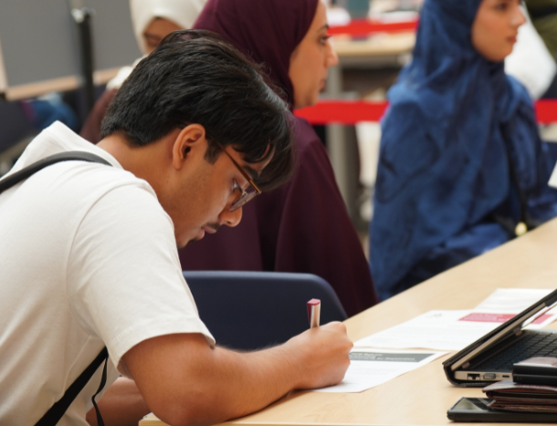 A student filling out paperwork at a desk during an orienation or registration session