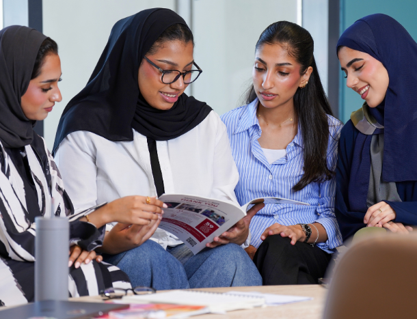 A group of female students gathered around a table looking at a university brochure.