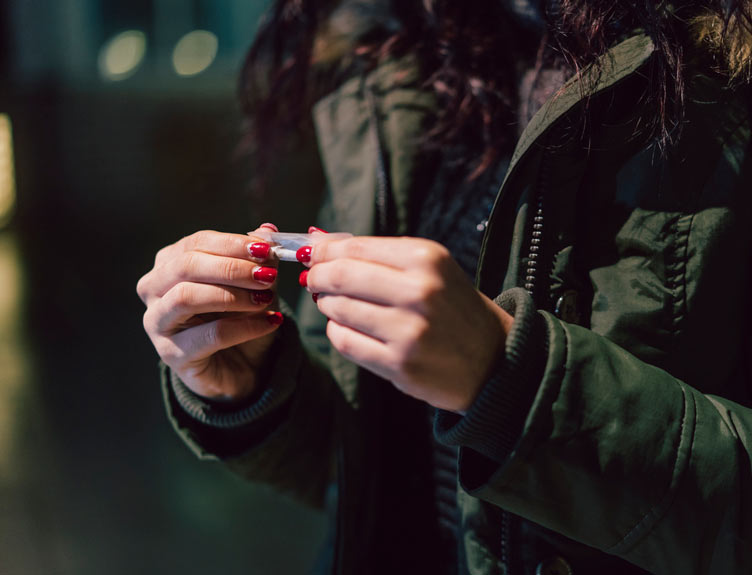 Young adult woman rolling a cigarette outdoor in the city at night 