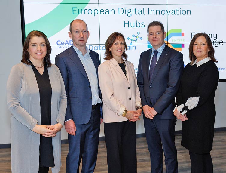 Five smartly dressed professionals pose for photo in front of digital screen.