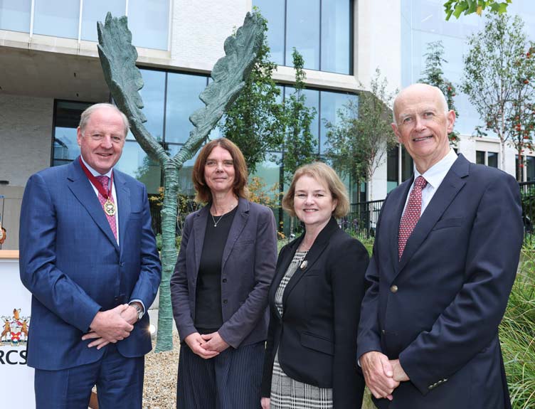 Four people standing outdoors in front of a modern building and the Beatha sculpture, posing for a group photograph.
