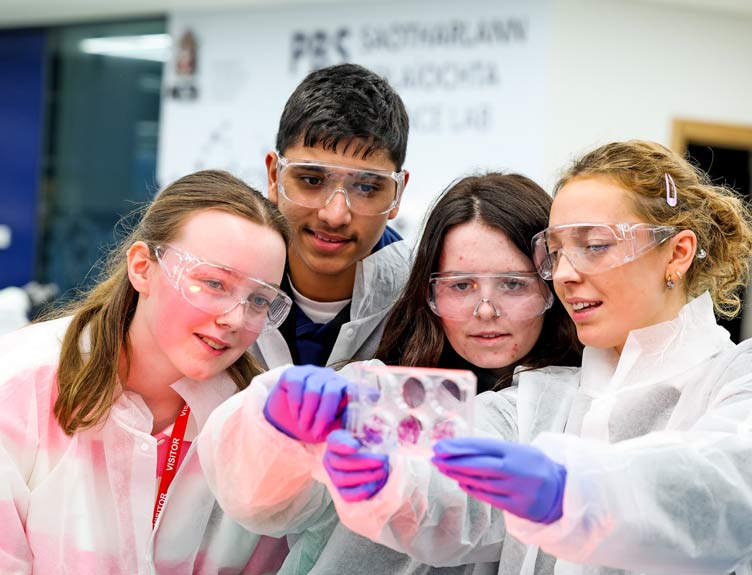 Four young people wearing white overalls in lab setting