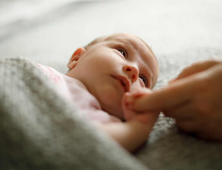 A newborn baby holding an adult's finger