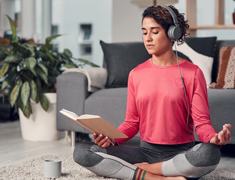 woman meditating at home with book and headphones