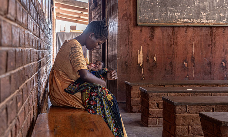 A Malawian mother holds her child while sitting on a bench.