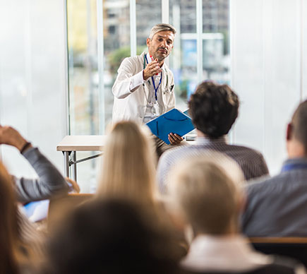 A doctor in a white coat addressing a classroom.