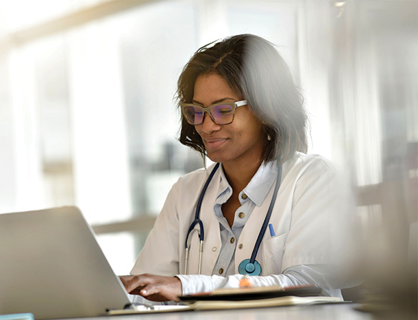 A doctor in a white coat works on a laptop