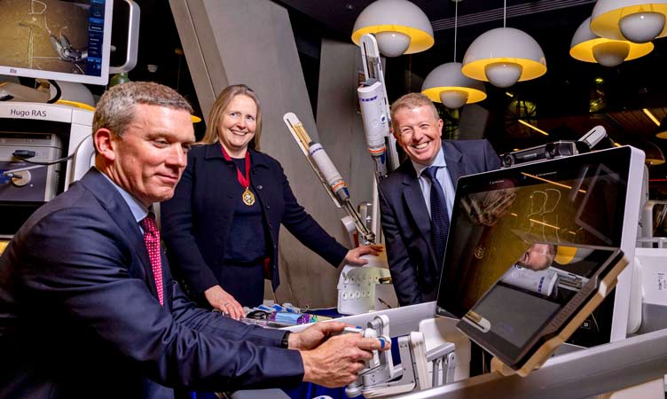 Three smiling people interact with medical robotics technology
