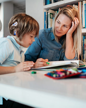 A mother helps their young son do their homework