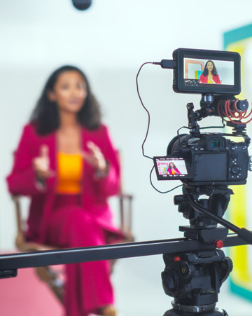 A host in a pink suit captured on a professional camera setup
