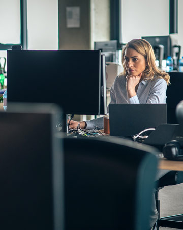 Businessperson using computer in empty office with desks without other coworkers.