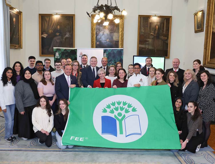 A group of people pose with a large green flag indoors