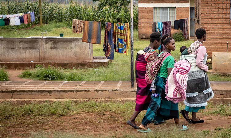 A group of women and babies walking past housing in Malawi.