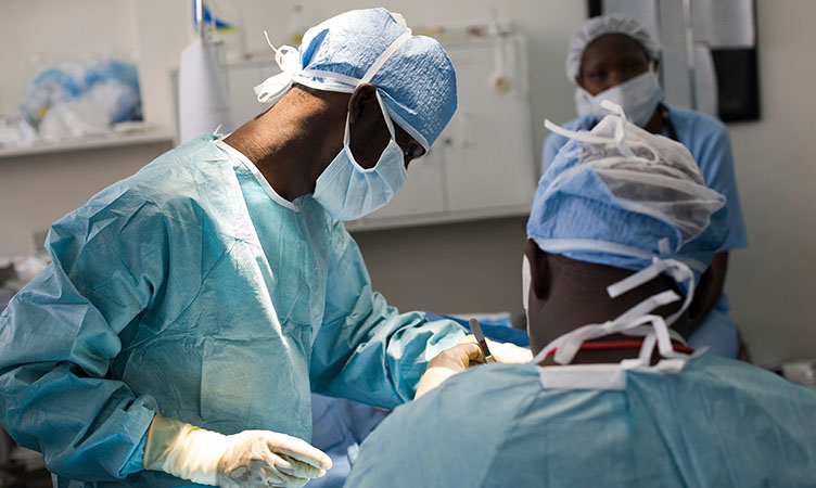 A group of three surgeons and medical professionals operating on a patient in theatre.