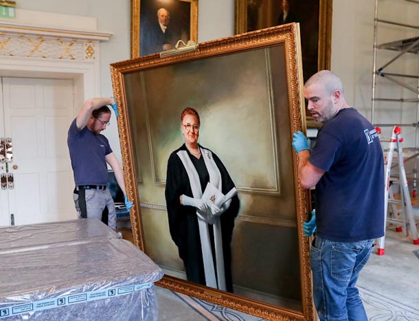 Two fitters hang a large portrait