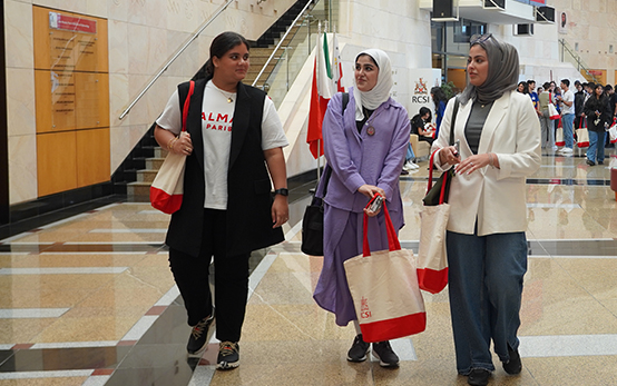 Three students walking through a university building while talking together, carrying study materials in a bright indoor corridor.