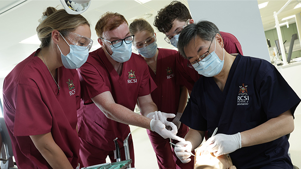 Prof. Albert Leung demonstrates a skill on a mannequin while a group of students in scrubs look on