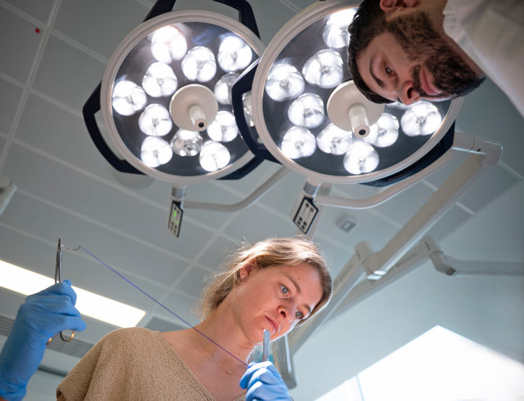Low-angle view of two people working under bright circular surgical lights in a clinical setting.