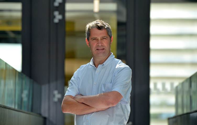 Professor folds arms and poses for photo within college building