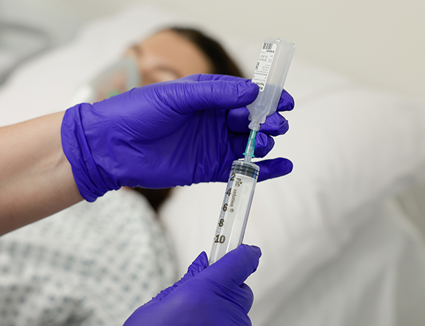 A closeup of a nurse inserting a syringe into medication