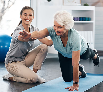  A physiotherapist assists a senior person with a yoga pose.