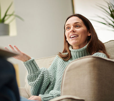 A person seated in an armchair in conversation and making a hand gesture.