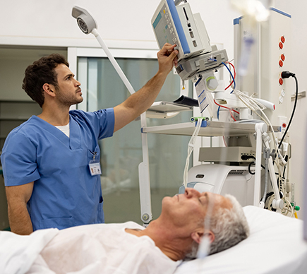 A medical professional operating digital equipment at a patient's bedside.