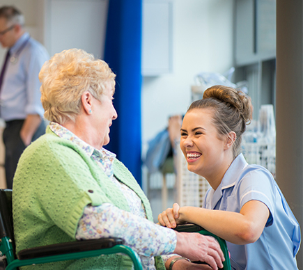 A nurse shares a joke with an elderly person in a wheelchair.