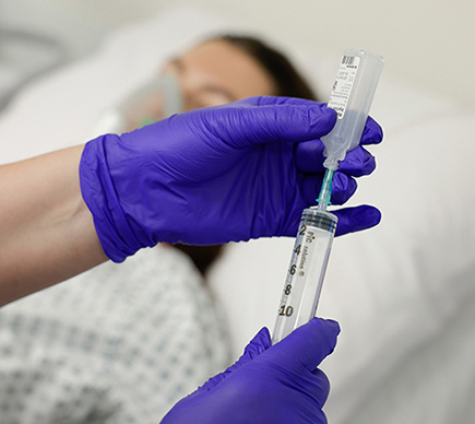 A closeup of a nurse inserting a syringe into medication
