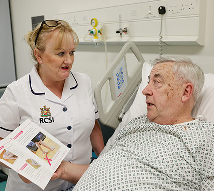A nurse speaks to an elderly patient in a hospital bed