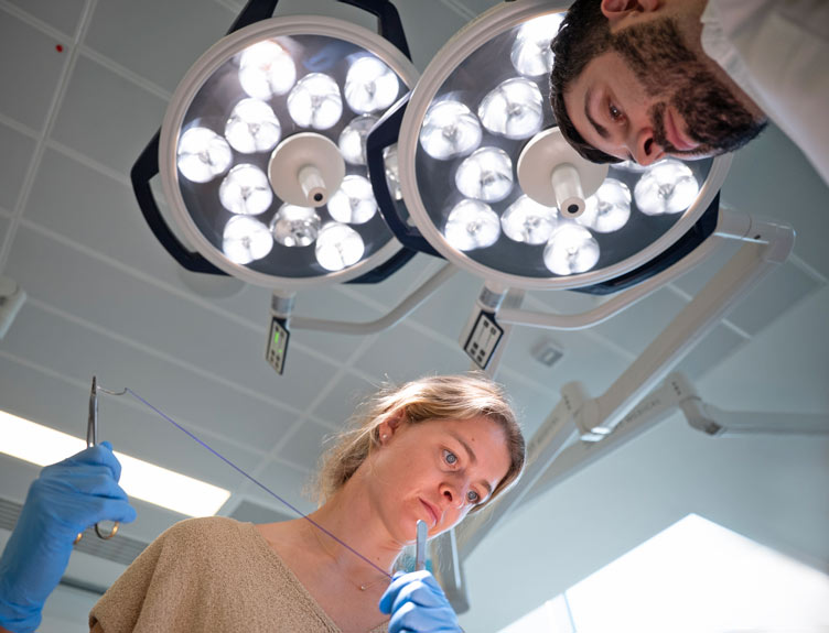 Dental training participants practising suturing techniques under surgical theatre lights.