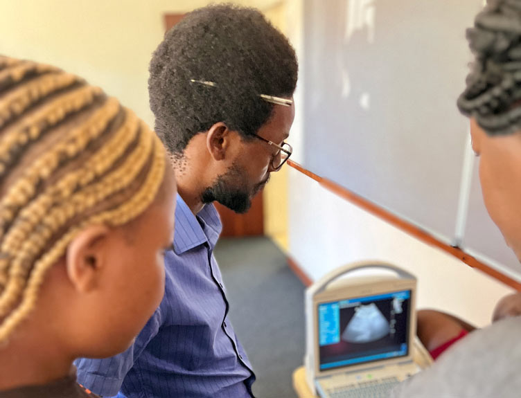 Three people pictured from behind looking at an ultrasound machine in a Malawi hospital